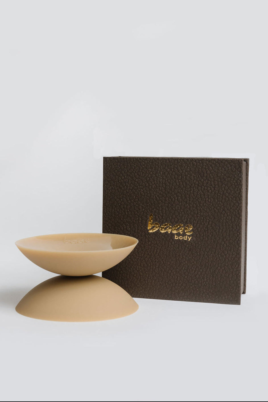 A beige silicone suction cup breast protector displayed in front of its dark brown textured packaging box with gold foil 'bear body' branding, set against a clean light gray background.